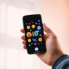 A smartphone screen displaying a colorful animated GIF with playful emojis and abstract shapes, held in a person's hand against a soft blurred background, modern and vibrant aesthetic