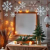 A cozy DIY New Year photo zone with handmade decorations: paper snowflakes hanging from the ceiling, a wooden frame with fairy lights, a festive table with pine branches, ornaments, candles, and a small Christmas tree, soft warm lighting, winter atmosphere, no people, no text